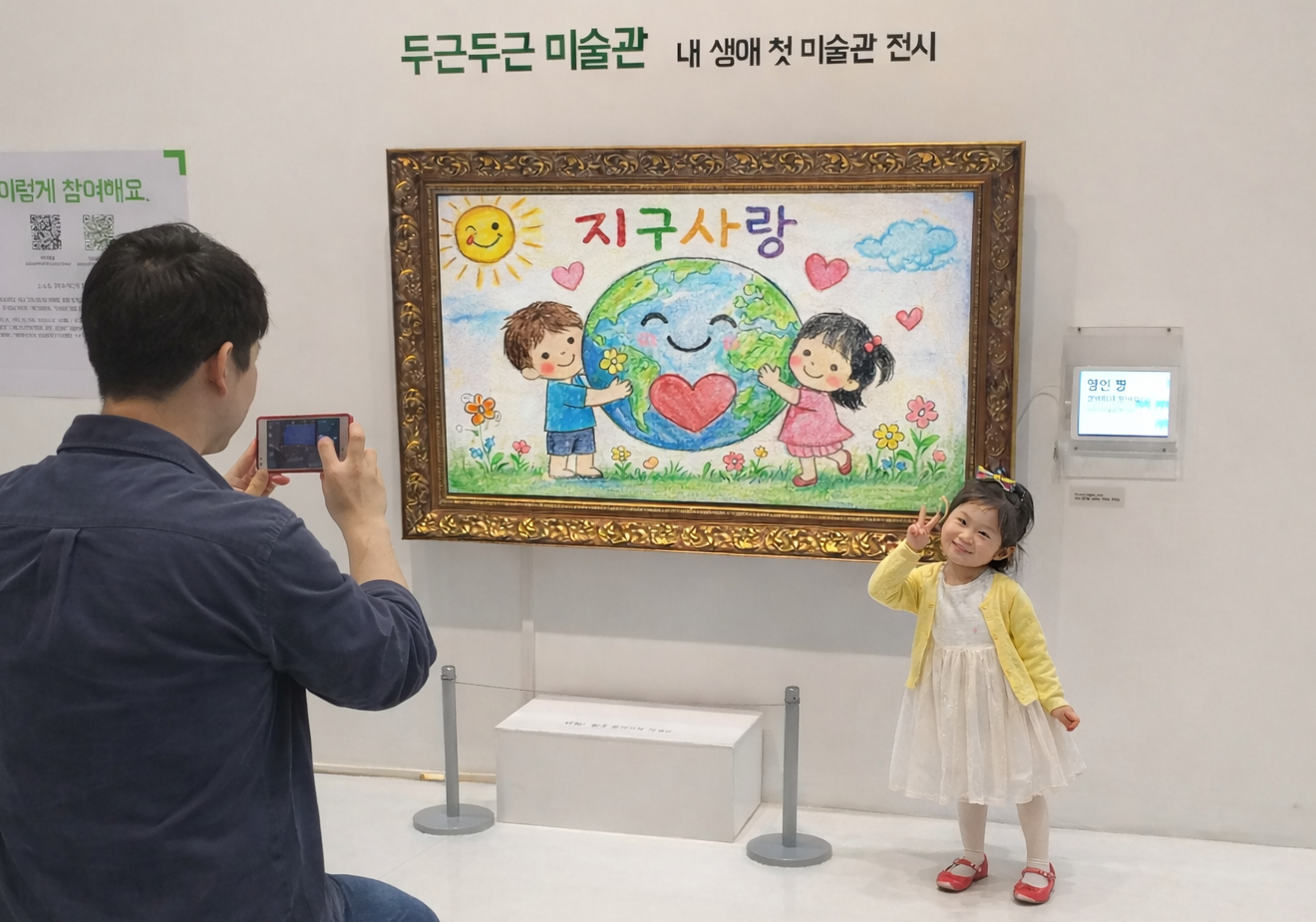 A child posing with their artwork displayed at a dgdgM exhibition