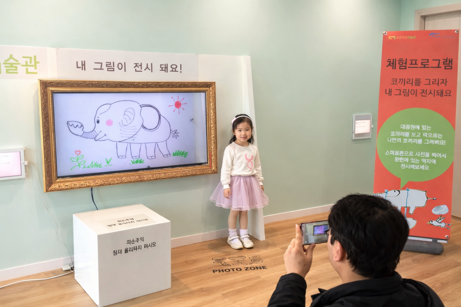 A child standing in front of their elephant drawing displayed on a digital frame